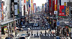 Strada affollata a Den-Den Town con insegne luminose e pedoni.