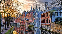 Canale pittoresco di Bruges al tramonto con edifici storici riflessi nell'acqua.