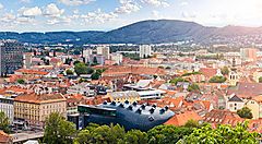 Vista panoramica della città di Graz con edifici e montagne sullo sfondo.