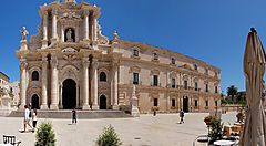 La cattedrale di Siracusa con cielo blu e persone in piazza.