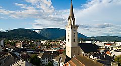 Vista panoramica di Villach con chiesa e montagne sullo sfondo.