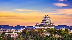 Il Castello di Himeji al tramonto, circondato da colline e cielo colorato.