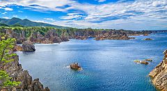 Costa rocciosa dell'isola di Sado con mare blu e cielo sereno.