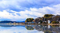 Borgo di Kitsuki riflesso nell'acqua sotto un cielo nuvoloso.