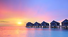 Bungalow sull'acqua alle Maldive con tramonto colorato.