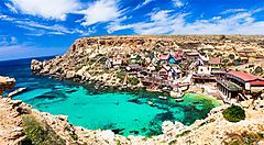 Baia con acque turchesi e case colorate a Malta.