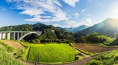 Paesaggio rurale a Takachiho con campi verdi e ponte sotto un cielo azzurro.