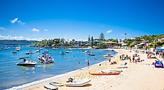 Spiaggia affollata a Watsons Bay con barche sul mare e case sullo sfondo.