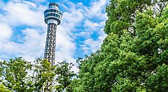 Torre Marine di Yokohama circondata da alberi verdi sotto un cielo azzurro.