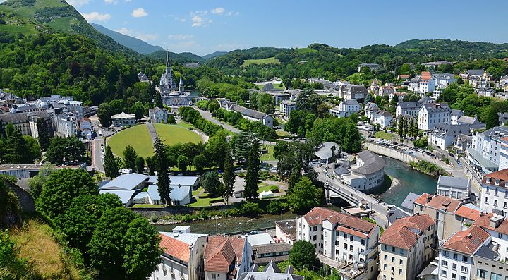 Veduta panoramica di Lourdes con edifici e paesaggio montano.