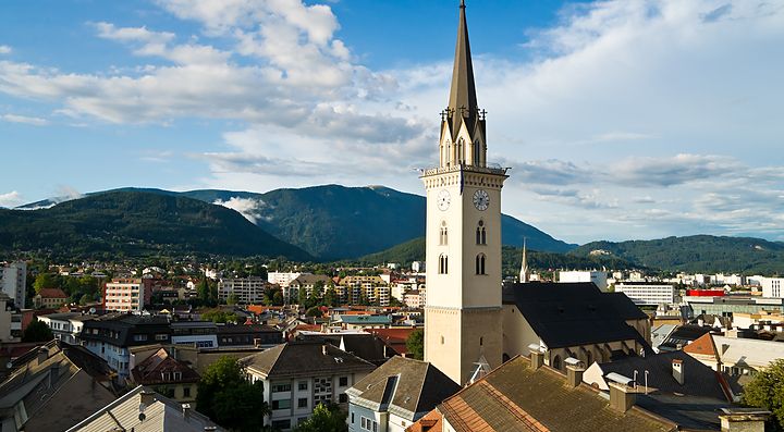 Vista panoramica di Villach con chiesa e montagne sullo sfondo.
