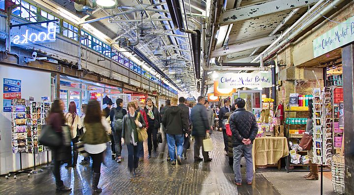 Persone passeggiano in una food hall a New York, circondati da negozi e bancarelle.