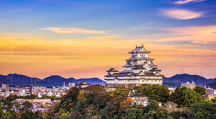 Il Castello di Himeji al tramonto, circondato da colline e cielo colorato.