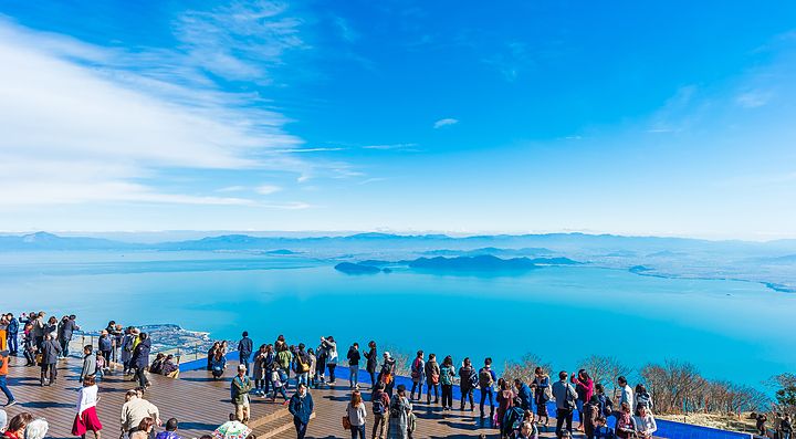 Visitatori osservano il Lago Biwa da un punto panoramico, cielo sereno.