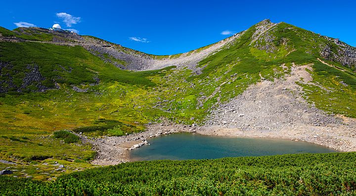 Lago ai piedi del Monte Norikura circondato da montagne verdi e cieli blu.