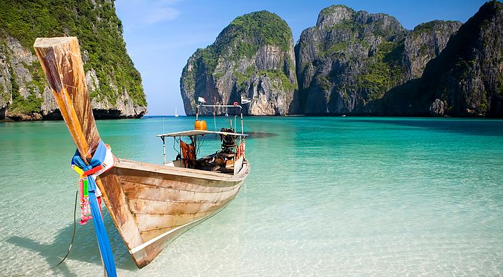 Barca tradizionale sulle acque turchesi di Phi Phi Island, con scogliere in lontananza.