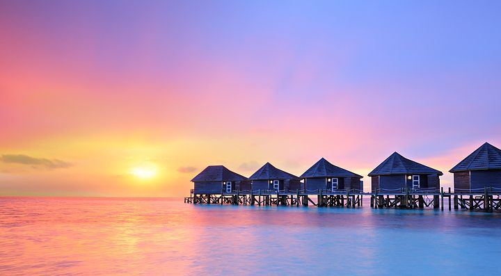 Bungalow sull'acqua alle Maldive con tramonto colorato.