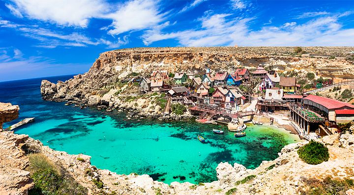 Baia con acque turchesi e case colorate a Malta.