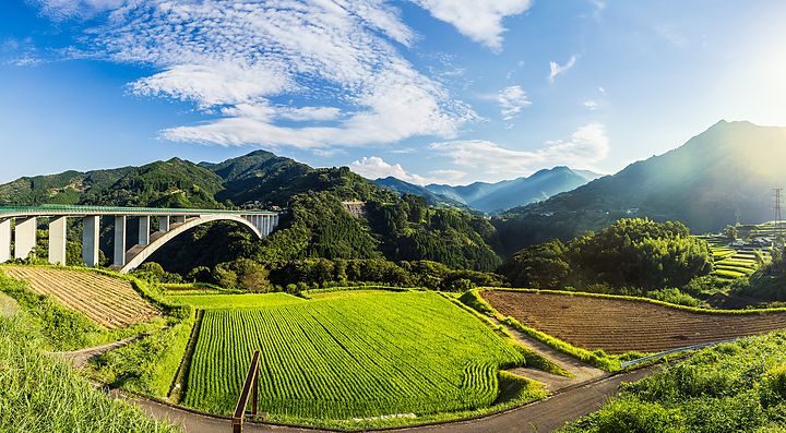 Paesaggio rurale a Takachiho con campi verdi e ponte sotto un cielo azzurro.
