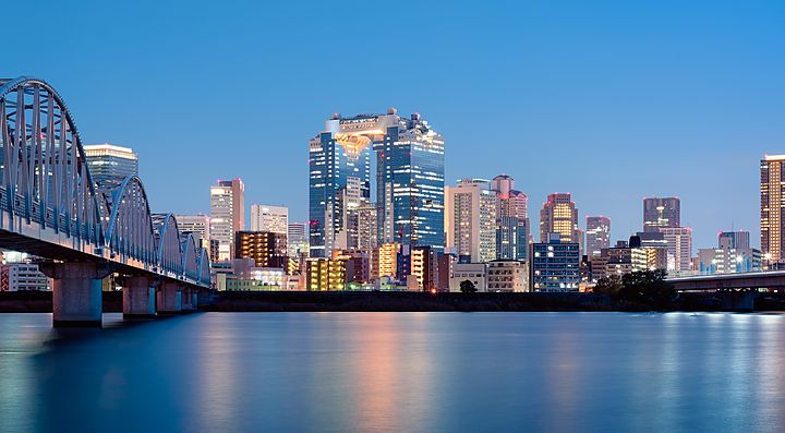Grattacieli illuminati di Umeda a Osaka, con ponte e fiume in primo piano.