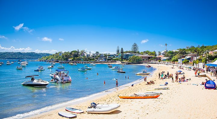 Spiaggia affollata a Watsons Bay con barche sul mare e case sullo sfondo.
