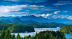 Paesaggio montuoso canadese con foreste e laghi sotto un cielo blu.