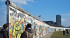 Persone osservano i graffiti sul Muro di Berlino in una giornata soleggiata.