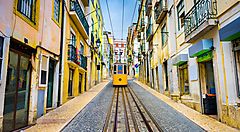 Un caratteristico tram giallo percorre una strada di Lisbona tra edifici colorati.