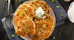 Piatto di frittelle di patate speziate con panna acida e cipollotto.