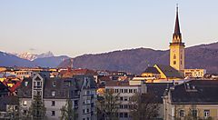 Veduta di una città austriaca con chiesa e montagne sullo sfondo.