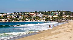 Spiaggia con turisti e onde, case in lontananza, Messico.