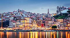 Porto al tramonto con edifici storici riflessi sul fiume Douro.