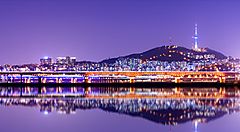 Skyline notturno di Seoul con torre Namsan illuminata e riflesso nel fiume.