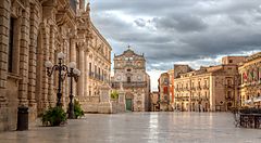 Piazza Duomo a Siracusa con edifici storici e cielo nuvoloso.