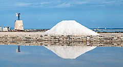 Veduta delle saline di Trapani con cumulo di sale e mulino sullo sfondo.