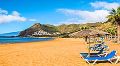 Spiaggia con lettini e ombrelloni, montagne e mare alle Canarie.