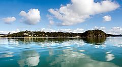 Paesaggio costiero in Nuova Zelanda con cielo blu e nuvole riflessi nell'acqua.