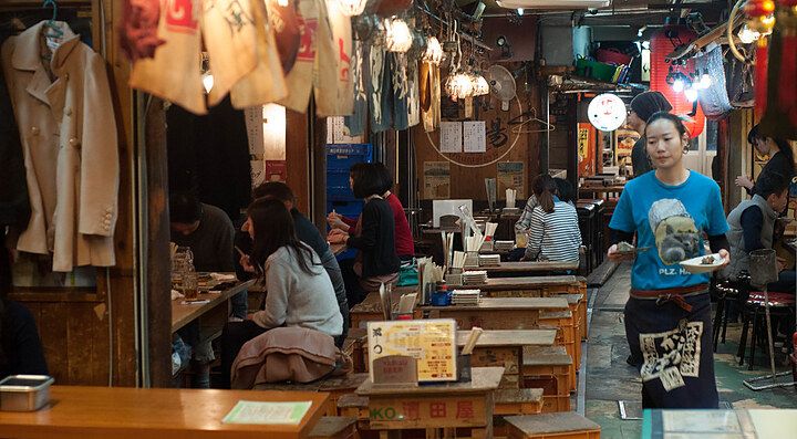 Ristorante giapponese affollato con tavoli in legno e cameriera che serve i clienti.
