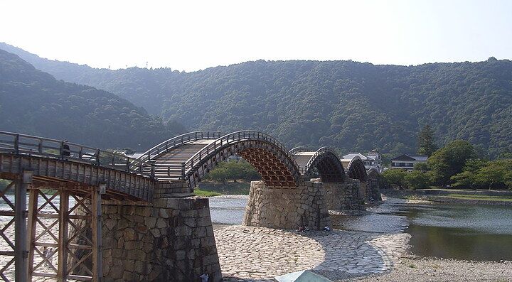 Ponte di legno a cinque arcate su un fiume, circondato da colline e vegetazione.