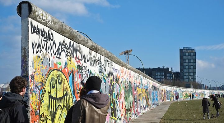Persone osservano i graffiti sul Muro di Berlino in una giornata soleggiata.