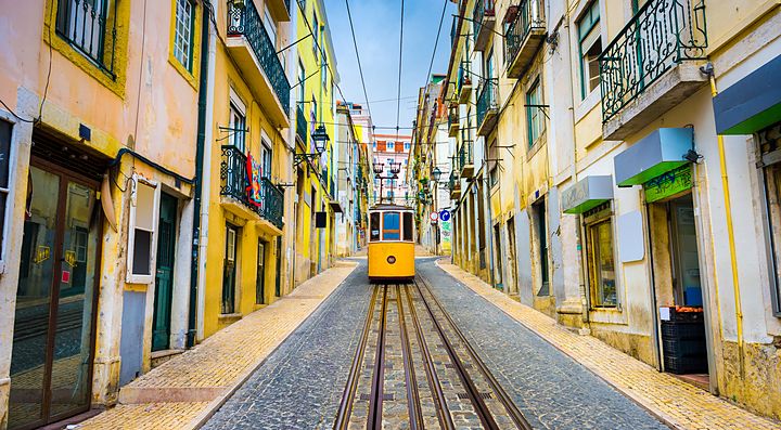 Un caratteristico tram giallo percorre una strada di Lisbona tra edifici colorati.