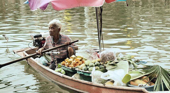 Una donna su una barca carica di frutta tropicale in un ambiente fluviale.