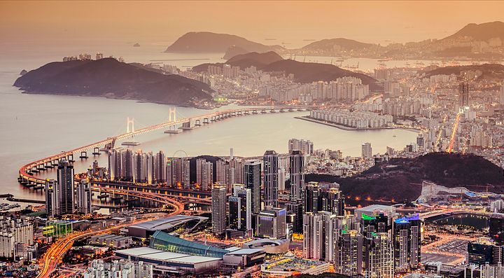 Panorama urbano di Busan con ponti e grattacieli al tramonto.