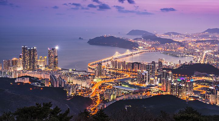 Veduta notturna della città di Busan illuminata con un ponte sul mare.