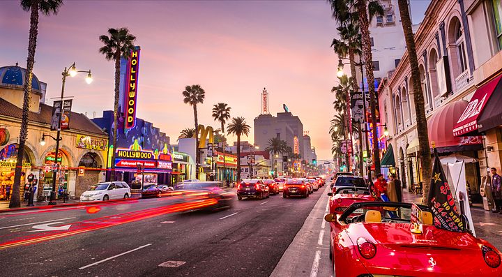 Strada trafficata di Los Angeles al tramonto con palme e insegne luminose.