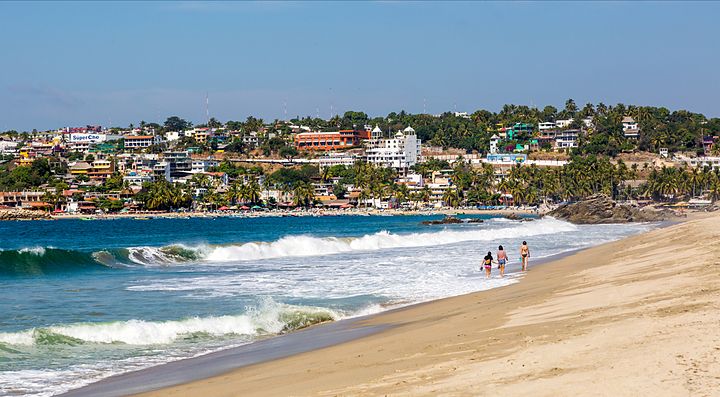 Spiaggia con turisti e onde, case in lontananza, Messico.