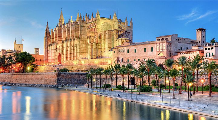 La Cattedrale di Palma di Maiorca illuminata al tramonto con palme lungo il lungomare.