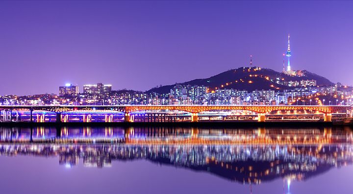 Skyline notturno di Seoul con torre Namsan illuminata e riflesso nel fiume.