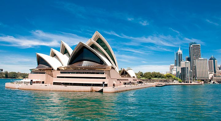 La Sydney Opera House vista dal mare con grattacieli sullo sfondo.