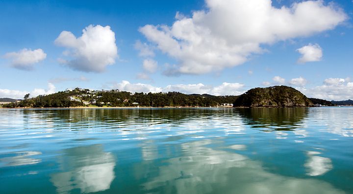 Paesaggio costiero in Nuova Zelanda con cielo blu e nuvole riflessi nell'acqua.